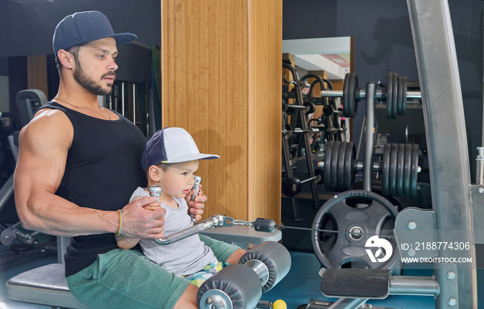 Side view of dad and little son doing arms exercises sitting on gym simulator.