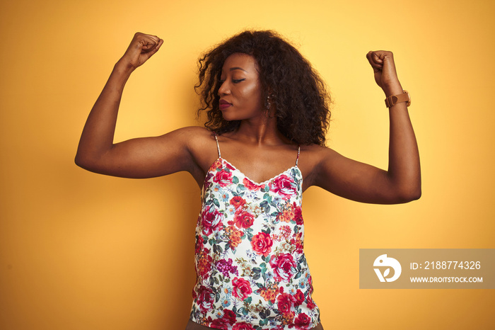 African american woman wearing floral summer t-shirt over isolated yellow background showing arms muscles smiling proud. Fitness concept.