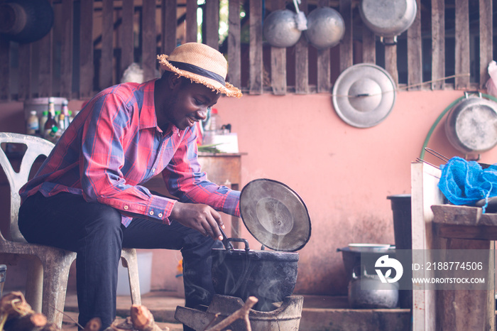 African man sitting to blow fire to cook food