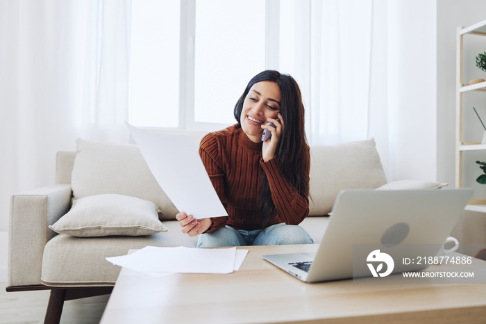 A woman at home sits in front of her laptop and pays her utility bills while talking on the phone, online technology for comfort in life