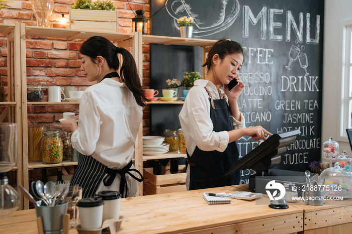 Beautiful skilled entrepreneur dressed in apron with mock up making coffee business with partner. barista standing at bar counter and talking on cellphone with web consultant order food in cafeteria