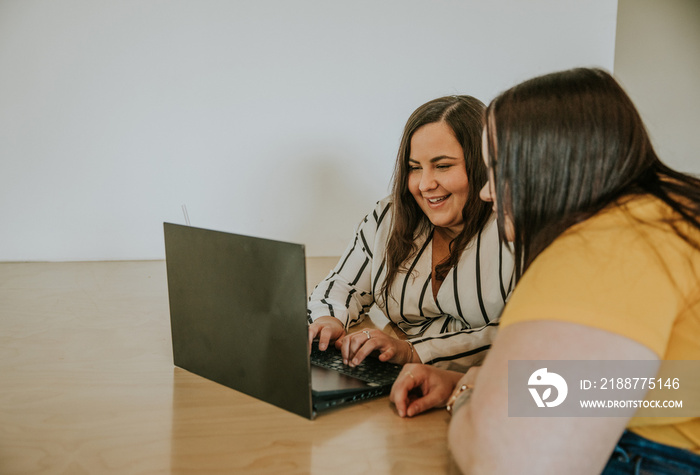 2 plus size women look at laptop and smile