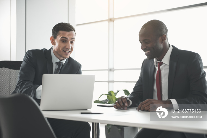 Business partners negotiating at the table. Caucasian man focused on laptop and african holding pen