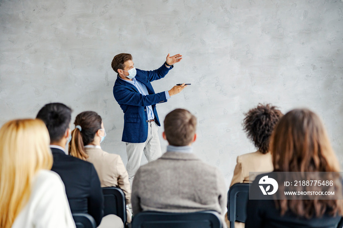 Futuristic business seminar and technology. A businessman standing in the boardroom with a smartphone in his hands and shoving a hologram while the audience sitting and listening.