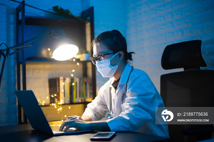 Asian woman doctor wearing protective face mask working and video call on a laptop overtime at home. WFH. Work from home for avoid the Coronavirus COVID 19 concept.