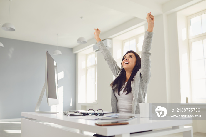 Happy successful smiling business woman raised her hands up while sitting at a table in the office.