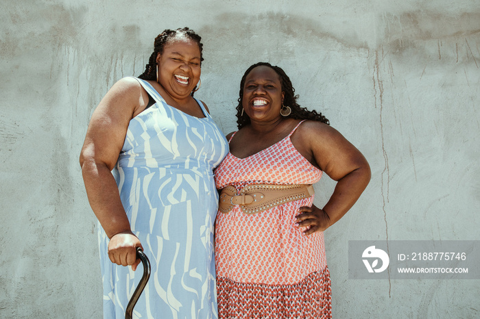 2 African American women stand against a textured backdrop smiling together