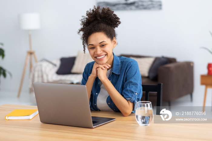 Online education. Portrait of smiling young female freelancer or employee working in co-working or modern office or home. African American woman using laptop computer looking at the camera, smiling