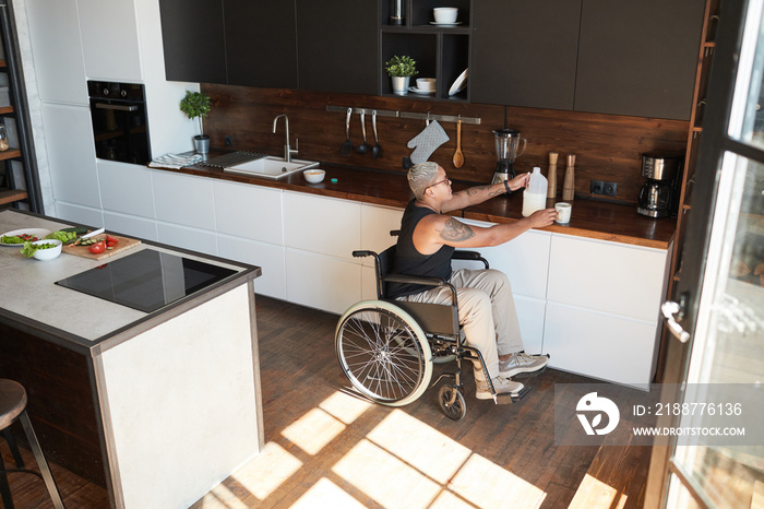 Wide angle shot of contemporary tattooed woman in wheelchair making coffee at home lit by sunlight, copy space