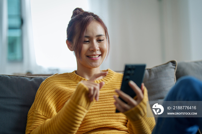 portrait of a young Asian woman woman holding smartphone while sitting on sofa