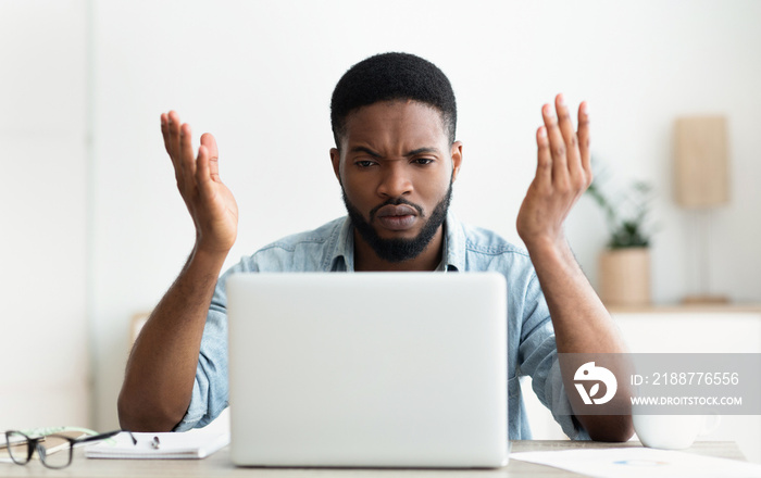 Stressed african-american businessman looking at laptop screen in modern office