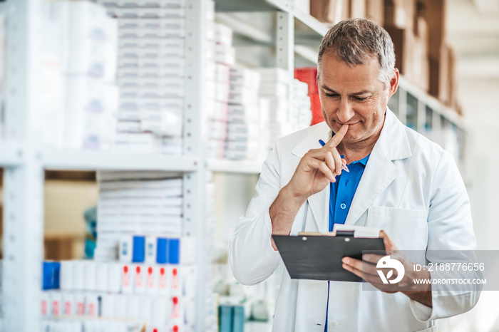 Smiling American man pharmacist or Chemist Writing On Clipboard While standing in interior of pharmacy. Professional pharmacist with clipboard in modern drugstore