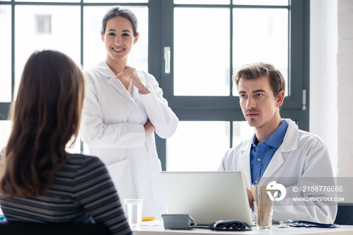 Young nurse listening to an experienced physician while consulting a female patient in the office of a modern hospital