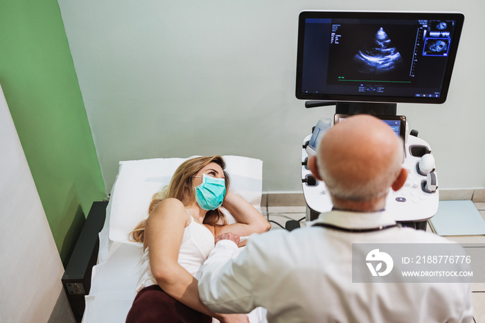 Experienced senior doctor performs a cardiac examination on a young female patient. He is using cardiology scanner. Medicine and modern technology concept.