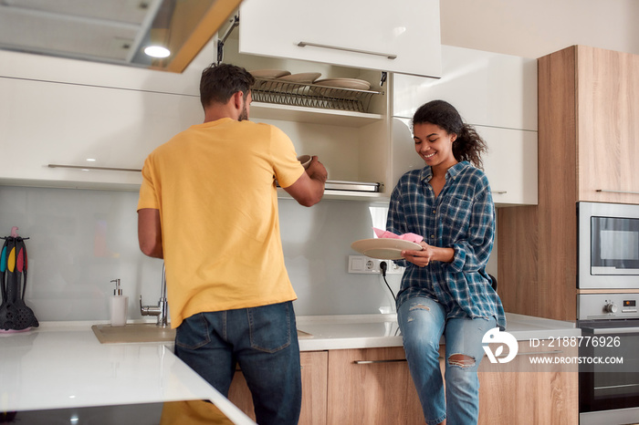 A clean home is a happy home. Happy multicultural couple in casual clothes wiping the dishes and smiling while standing in their modern kitchen. Cleaning home