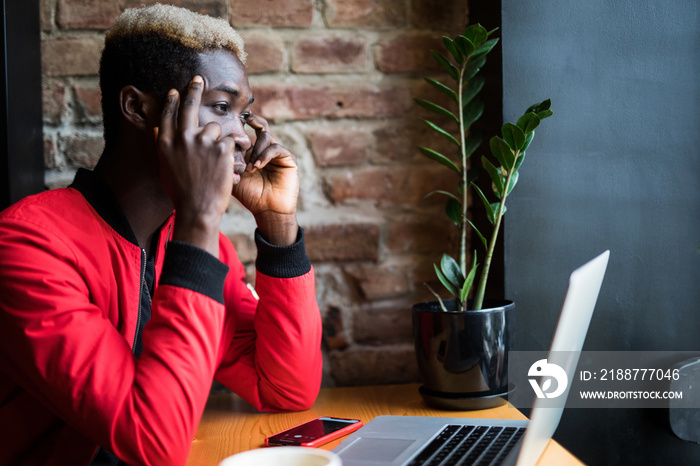 Young handsome Afro-American man using laptop and thinking while working in cafe