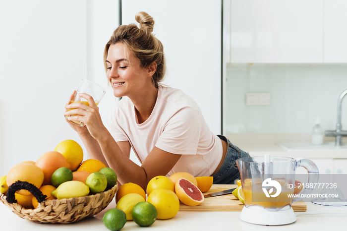 Woman drinking freshly squeezed homemade orange juice in white kitchen