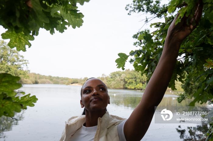 Portrait of woman touching leaves on tree by river