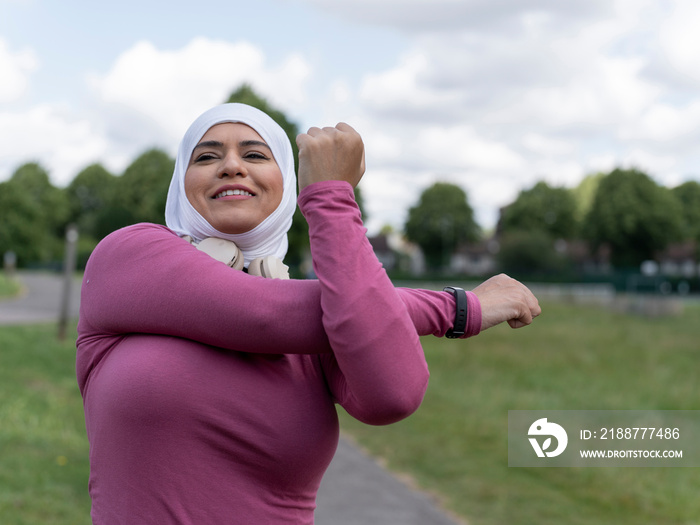 UK,Sutton,Woman in headscarf and sports clothing stretching in park