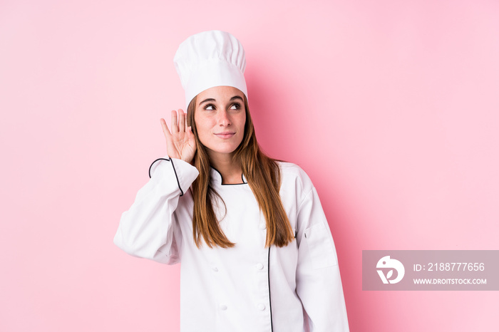 Young caucasian chef woman isolated trying to listening a gossip.