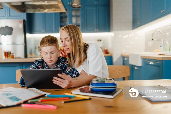 Mom and son using tablet computer while sitting in cozy kitchen