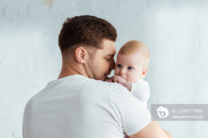 happy young man holding adorable baby boy on hands in bedroom