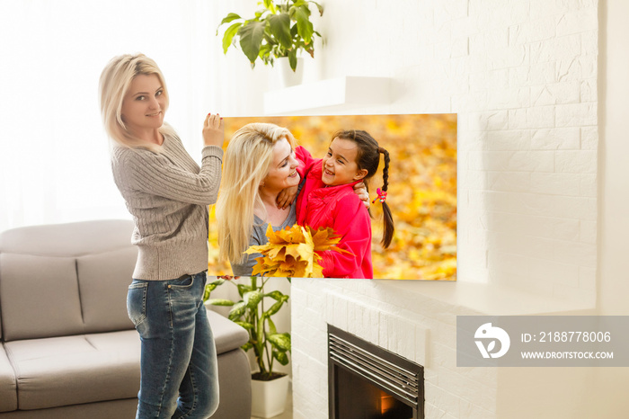 Happy blonde woman hanging picture with flowers on wall at home