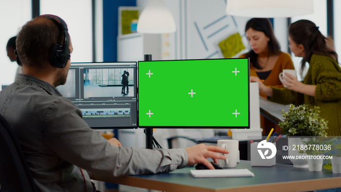 Man videographer with headset editing movie in post production software working at greenscreen, chroma key isolated display of computer. Video editor processing audio film montage in start up office