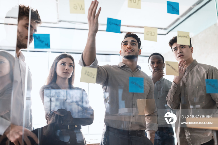 Diverse colleagues brainstorming using sticky post-it notes on glass wall