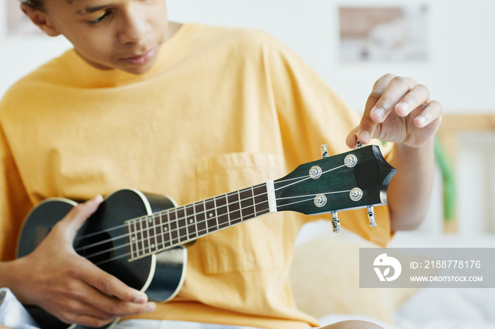 Minimal cropped shot of teenage boy playing ukulele while sitting on bed, copy space