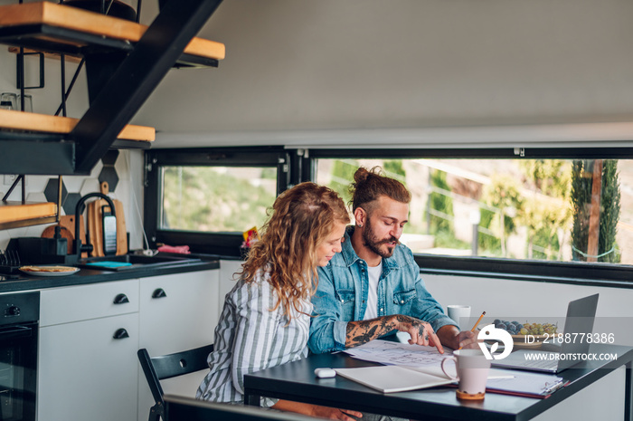 Happy couple using laptop and looking into blueprints of their new home