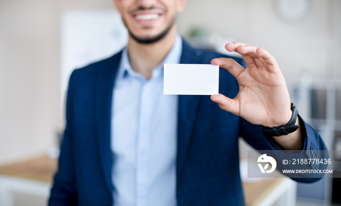 Cropped view of young Arab man showing empty business card with mockup for design at modern office