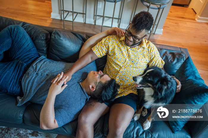 Gay male couple snuggling at home on couch together with their Australian Shepherd dog