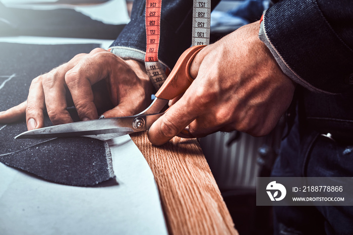 Fashion designer is cutting off fabric  with scissors.