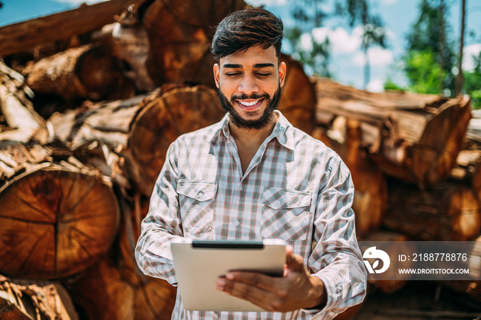 Portrait of Latin young man working on tablet beside tree trunks.