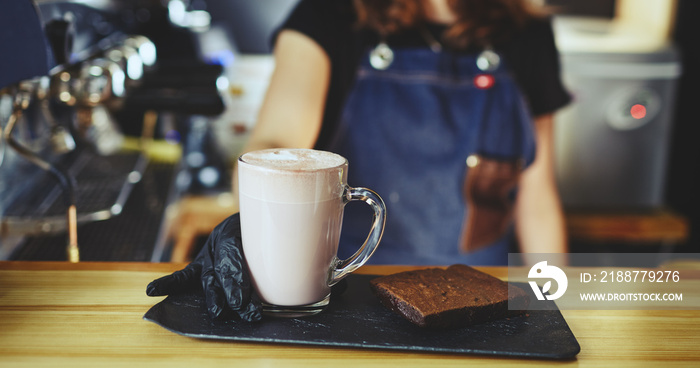 Barista wearing medical latex black gloves, making pink matcha latte with milk. Bartender preparing tasty drink and brownie cake.Blurred image,selective focus