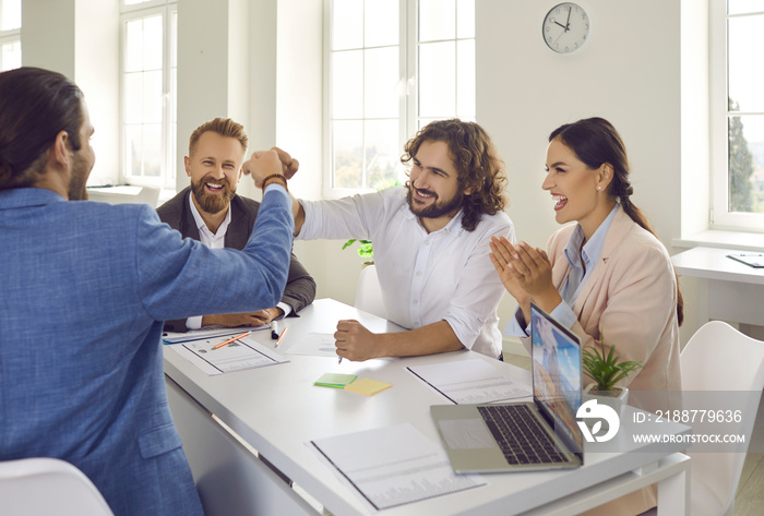 Business people making deal. Smiling coworkers fist bumping sitting at office desk with notebook PC in staff meeting. Employees do good job, complete work, finish successful project. Teamwork concept