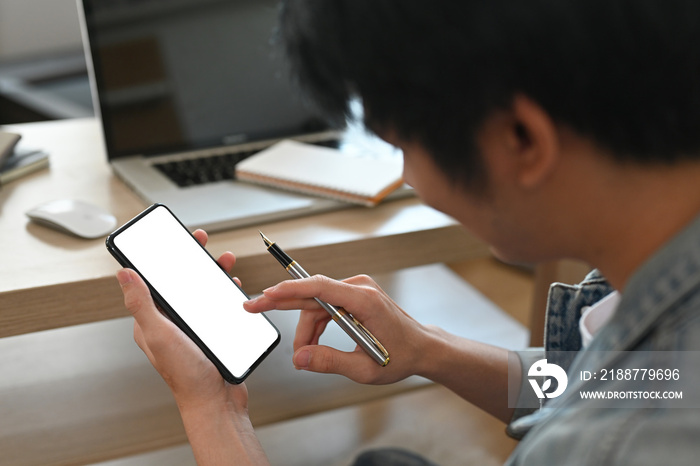 The shoulder close up with Asian man using a blank smartphone screen in the office home decoration. Business and financial concepts.