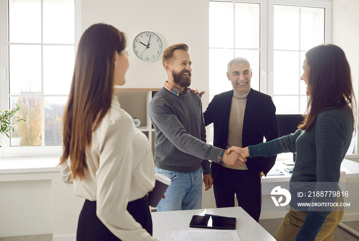 Happy business people meeting in a modern office. Two colleagues making an acquaintance and greeting each other. Friendly man and woman shaking hands after their coworkers have introduced them