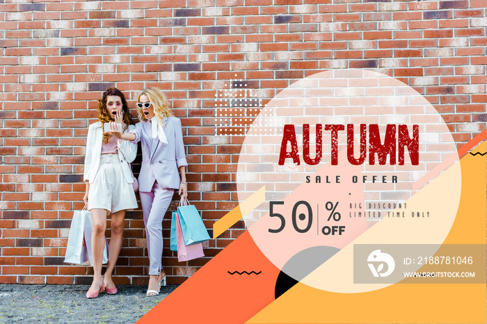 Shocked young women with shopping bags taking selfie while standing in front of brick wall, autumn sale banner