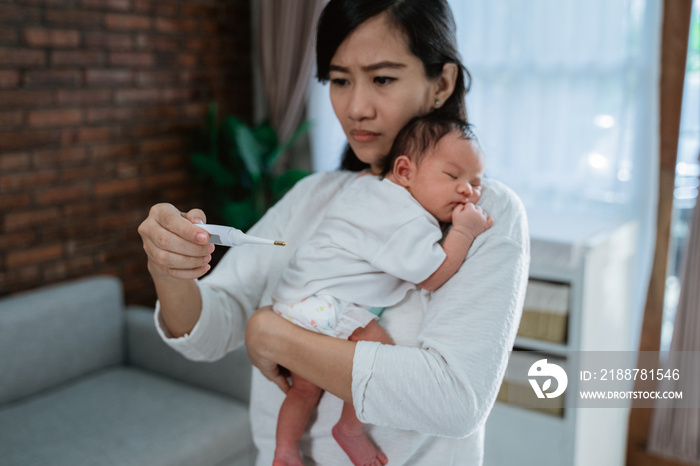 asian mother measuring temperature to her little baby daughter at home