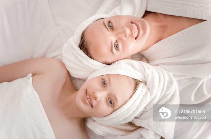 Happy family. Top view of delighted happy mother and daughter looking at you and smiling while lying together