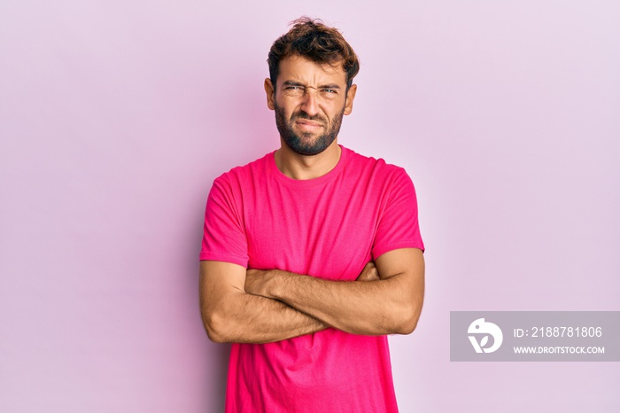 Handsome man with beard wearing casual pink tshirt over pink background skeptic and nervous, disapproving expression on face with crossed arms. negative person.