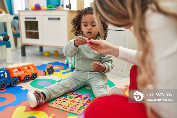 Teacher and toddler playing with maths puzzle game sitting on floor at kindergarten