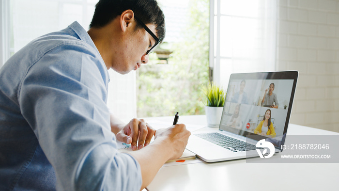 Young Asia businessman using laptop talk to colleagues about plan in video call meeting while work from home at living room. Self-isolation, social distancing, quarantine for corona virus prevention.