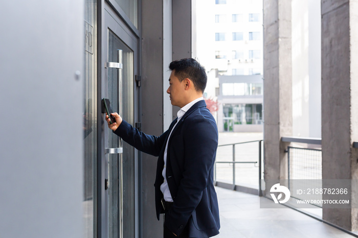 Successful Asian businessman opens the door of the office center using a smartphone and NFC application