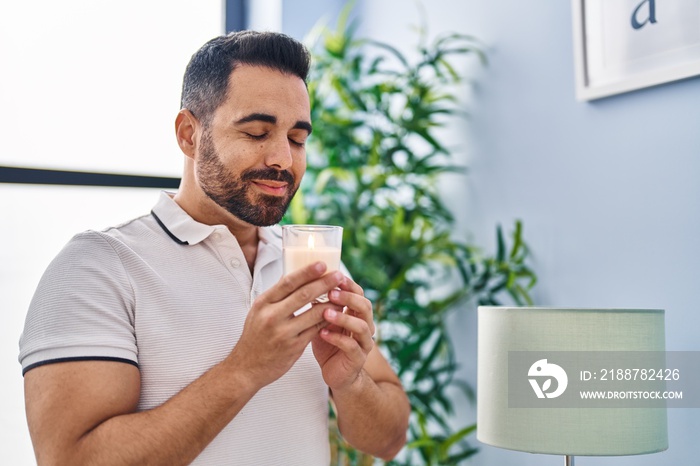 Young hispanic man smiling confident smelling candle at home