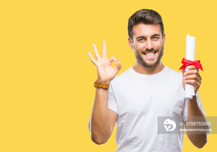 Young handsome man holding degree over isolated background doing ok sign with fingers, excellent symbol