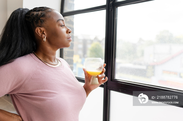 Woman holding glass while looking through window at home