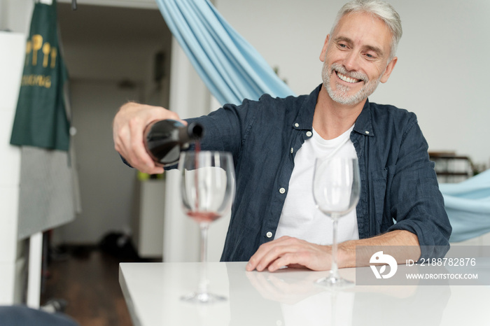 Mature man pouring red wine at home